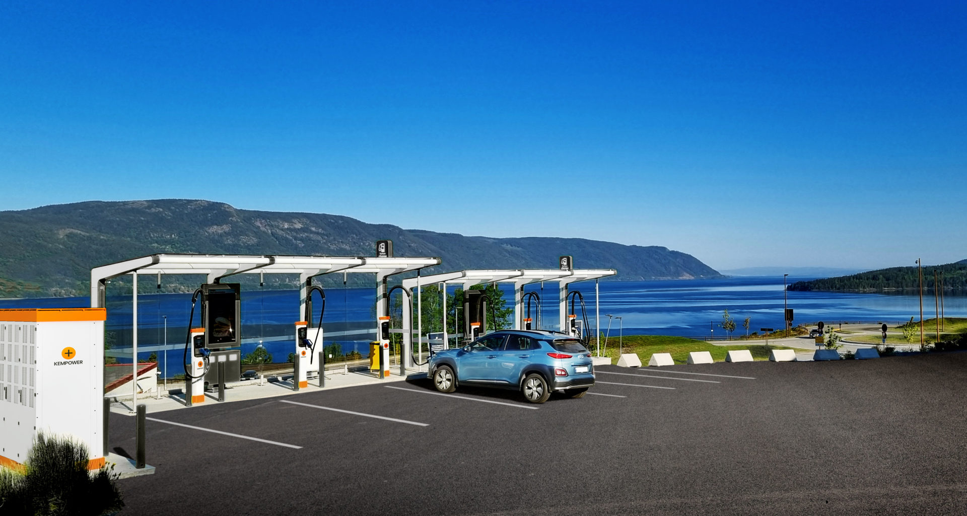 A car parked at a tranquil EV charging station with a breathtaking view of a serene lake and distant mountains under a clear blue sky.
