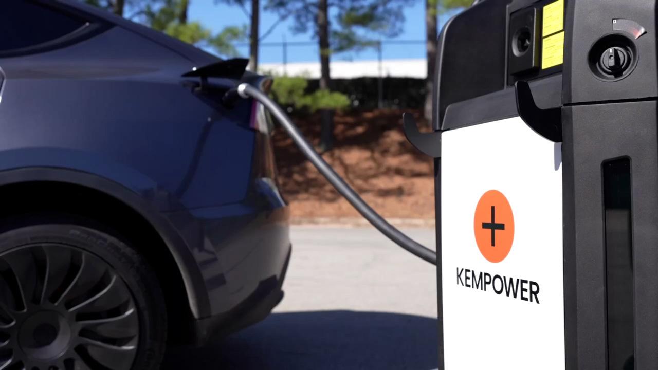 An electric car is connected to a kempower charging station, with the focus on the charging port and cable on the side of the vehicle.