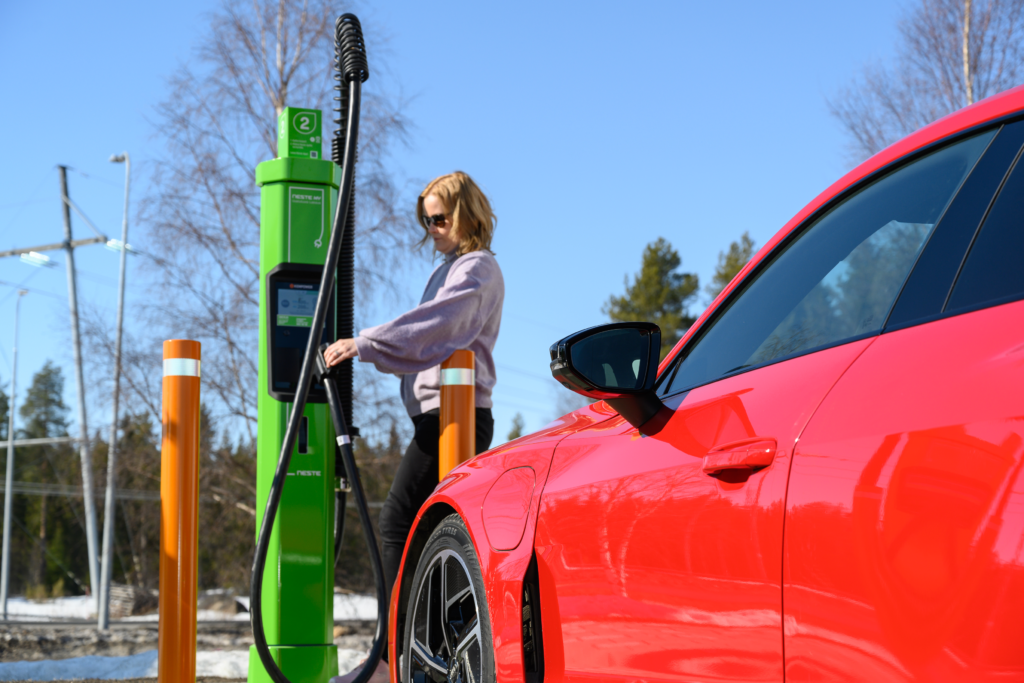 A person charging a red electric car at a charging station on a sunny day.
