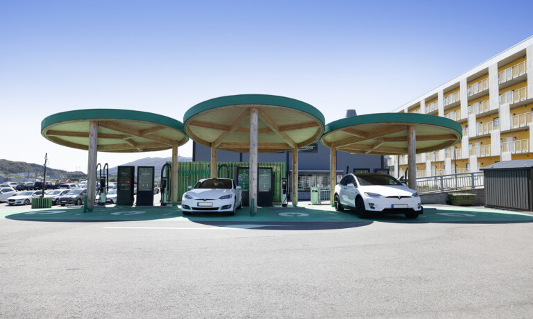 Two electric vehicles connected to charging stations under a contemporary style solar canopy on a sunny day, representing the electrification of traffic.